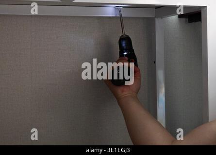 Man using power drill to assemble furniture frame at home, DIY furniture installation Stock Photo
