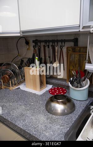 Kitchen countertop with knife block, cooking utensils, cutting boards and hanging kitchen tools on wall rack. Everyday domestic kitchen interior Stock Photo