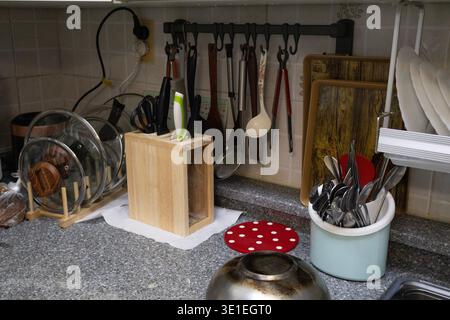 Kitchen countertop with knife block, cooking utensils, cutting boards and hanging kitchen tools on wall rack. Everyday domestic kitchen interior Stock Photo