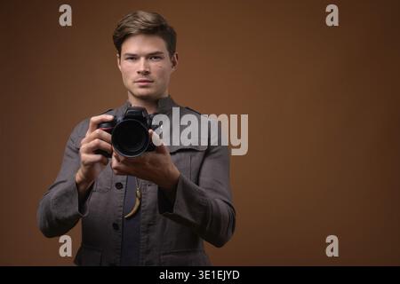 Studio shot of young handsome man wearing denim jacket against brown background Stock Photo