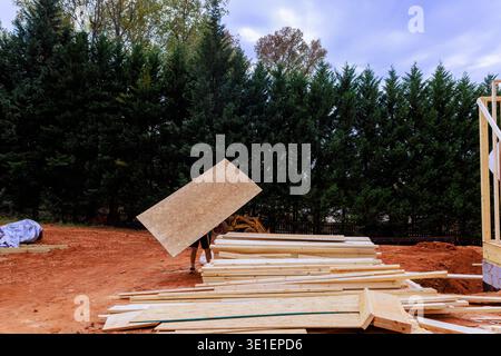Framing worker carries wooden osb board at construction site with piles Stock Photo