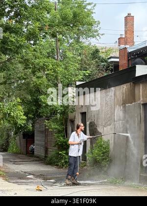 Man removing graffiti from a street wall with a high-pressure water hose in Montreal, Canada Stock Photo