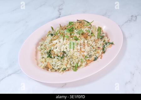 A serving of "kampung" fried rice mixed with green vegetables and topped with crispy fried shallots, presented on a pale pink oval plate against a whi Stock Photo