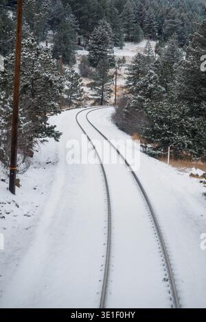 A train track winds through a snow-covered forest, suggesting a journey through a winter landscape. Stock Photo