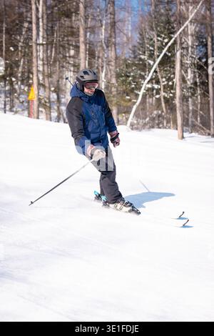 An elder skier in blue makes a dynamic turn on a snowy slope bordered by red safety netting Stock Photo
