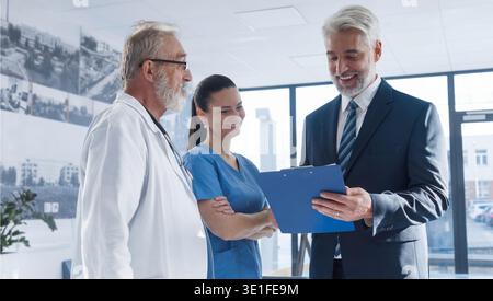Medical sales representative presenting new medication to doctors, standing hospital hallway. Stock Photo
