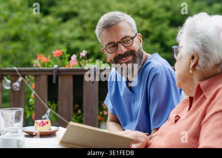Caregiver spending time with elderly woman, reading book. Stock Photo