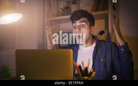Excited man working late at home on laptop Stock Photo