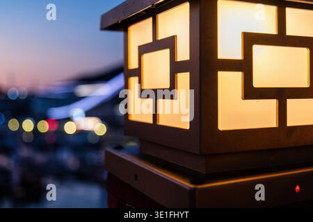 Warm glowing geometric lantern illuminates a serene evening. Urban bokeh lights create a peaceful atmosphere, perfect for design or travel themes Stock Photo
