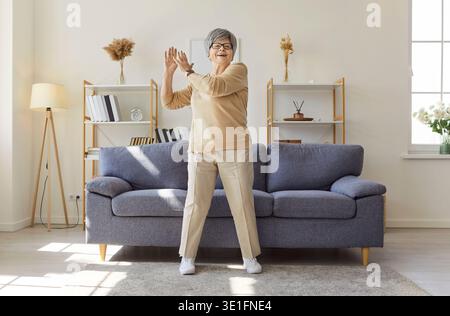Happy senior woman doing stretching exercises at home, active workout and warmup Stock Photo