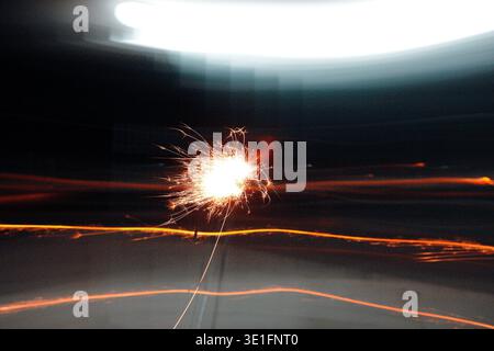 Long-exposure capture of sparkler bursting in night darkness, creating radiant golden light trails and glowing core against blurred background. Stock Photo