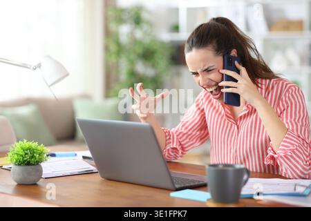 Angry self employed talking on phone and complaining working at home Stock Photo