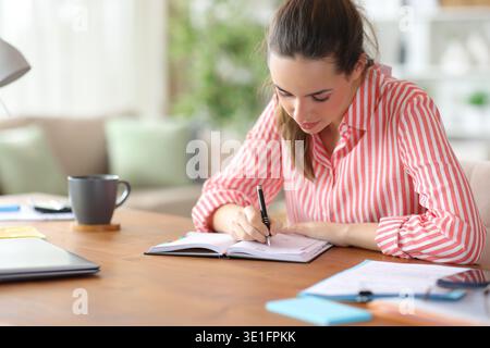 Serious freelance worker writing notes in paper agenda working at home Stock Photo