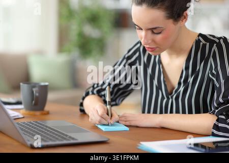 Self employed writing in blue sticky note on a wooden table working at home Stock Photo