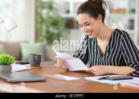 Happy self employed reading paper letter in a wooden table while working at home Stock Photo