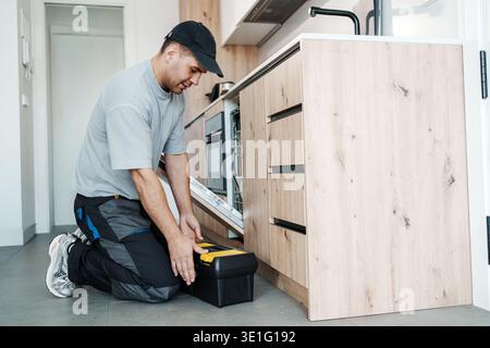 Hispanic Technician Repairing Plumbing System. Technician Fixing Leaking Pipes Under Kitchen Cabinet Stock Photo