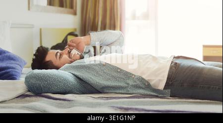 Young man talking on mobile phone while relaxing in bed Stock Photo