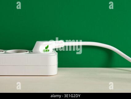 White eco labeled power plug connected to extension socket on green background symbolizing clean energy and sustainability Stock Photo