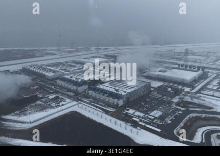 Aerial view of a large modern data center complex covered in snow, emitting steam from cooling units during winter, Eemshaven, Netherlands. Stock Photo