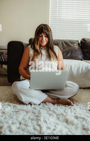 Woman working remotely from home sitting on floor Stock Photo