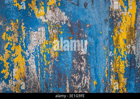 Colorful weathered wall surface with peeled blue,white and yellow paint, random scratches on concrete wall background. Grunge weathered distressed abs Stock Photo