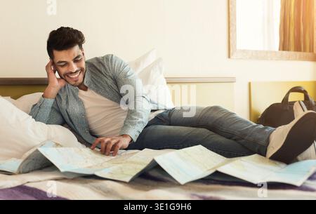 Young arabic man traveller lying on bed and studying map Stock Photo