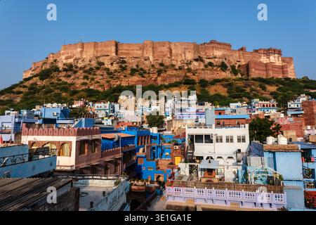 Brightly painted blue and white houses of Jodhpur stand at the foot of the steep cliff supporting the expansive Mehrangarh Fort complex. Stock Photo