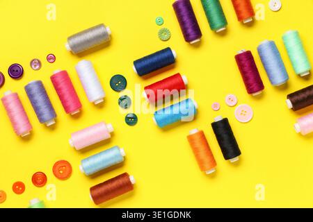Composition with many different thread spools and buttons on yellow background Stock Photo