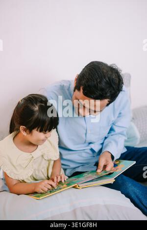 A father and daughter reading a children's book together in a cozy home environment. Stock Photo