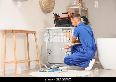 Male plumber repairing washing machine in bathroom Stock Photo