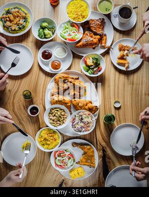 Shared Feast On Rustic Wooden Table. Lively Community Meal Featuring Fried Chicken And Fresh Salads Stock Photo