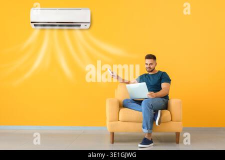Young man with laptop switching on air conditioner at home Stock Photo