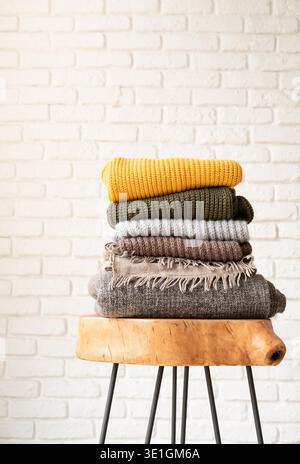 Hello fall. Cozy warm image. Stack of autumn warm sweaters on modern coffee table, white brick wall background Stock Photo