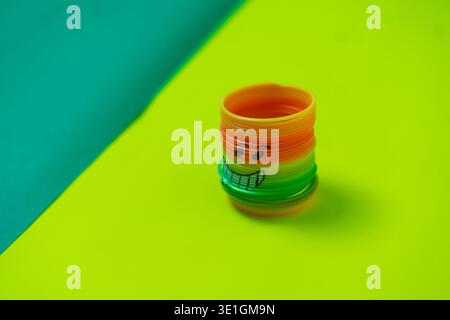 A vibrant rainbow-colored spring toy with a cheerful hand-drawn smiley face sits on a bright green background. This playful object evokes childhood no Stock Photo