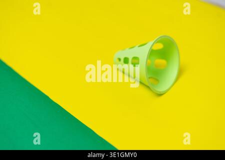 A bright green plastic shuttlecock skirt rests on a vibrant yellow surface with a diagonal green section. This colorful and abstract composition offer Stock Photo
