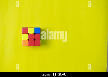 A vibrant logic puzzle cube featuring red, yellow, blue, and orange blocks rests on a bright yellow background. This playful image offers ample copy s Stock Photo