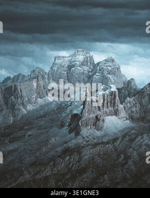 View of majestic, gray rocky mountains rise under a stormy sky, their peaks dusted with snow, creating a dramatic contrast of light and shadow, Cortin Stock Photo