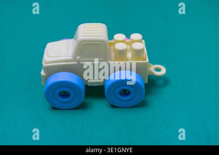 A vibrant, light yellow plastic toy truck with striking blue wheels stands out against a smooth, solid teal background, perfect for themes of childhoo Stock Photo