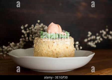 A beautifully decorated cake with a buttercream rose and green leaves on top, placed on a rustic wooden table. A charming dessert perfect for spring c Stock Photo