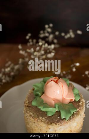 A beautifully decorated cake with a buttercream rose and green leaves on top, placed on a rustic wooden table. A charming dessert perfect for spring c Stock Photo