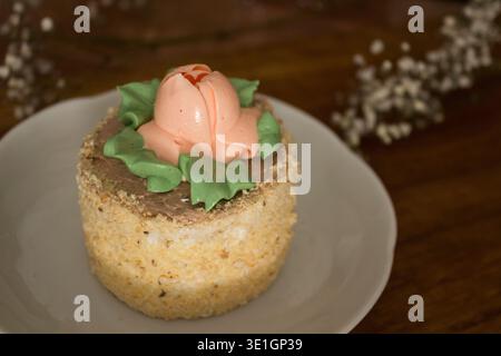 A beautifully decorated cake with a buttercream rose and green leaves on top, placed on a rustic wooden table. A charming dessert perfect for spring c Stock Photo