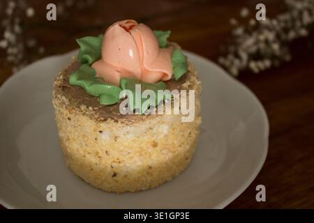 A beautifully decorated cake with a buttercream rose and green leaves on top, placed on a rustic wooden table. A charming dessert perfect for spring c Stock Photo