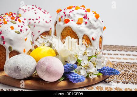A festive arrangement of beautifully decorated Easter cakes, colorful eggs, and delicate spring blossoms on a rustic embroidered cloth Stock Photo