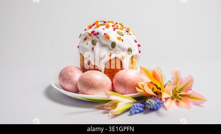 A festive Easter kulich cake is presented with marbled pink eggs and delicate spring blossoms on a clean white background Stock Photo