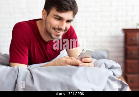 Handsome man using smartphone while lying in bed Stock Photo