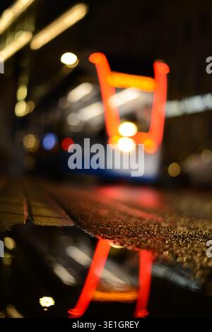 Europe. night. The glowing lights of the night train tram are reflected in a puddle. Blurred background focus on asphalt. Photo after the rain. vertic Stock Photo