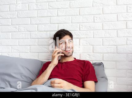 Happy man lying on bed and talking on smartphone Stock Photo