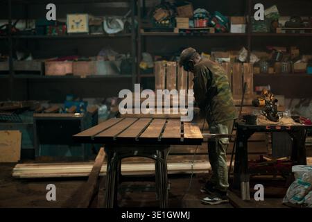 Factory contrasting lighting of a working workshop. Beautiful gloomy photo of a factory worker in a mask and uniform standing at a table operating a g Stock Photo