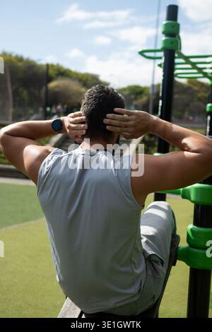 Young athletic man doing sit-ups during outdoor workout in a park. Fitness training, healthy lifestyle and strength exercise in natural environment. Stock Photo