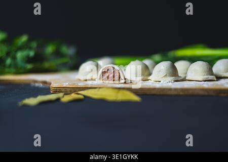Side view on the kitchen board Several dumplings in flour. The dumplings are cut in half and showcase beautiful ground beef. kitchen board on a dark b Stock Photo